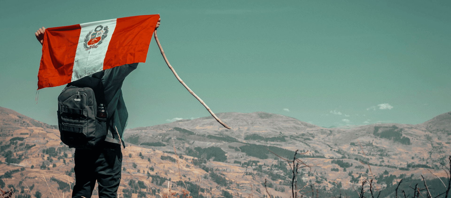 Traveler holding a Peruvian flag overlooking the Andean highlands.