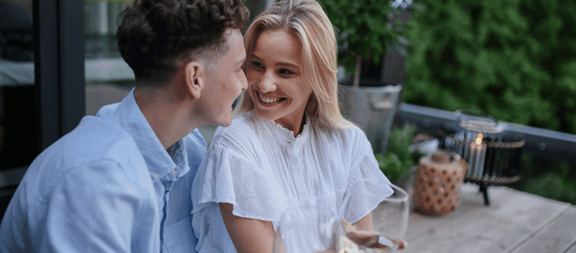 Couple smiling at each other while sitting together outdoors.