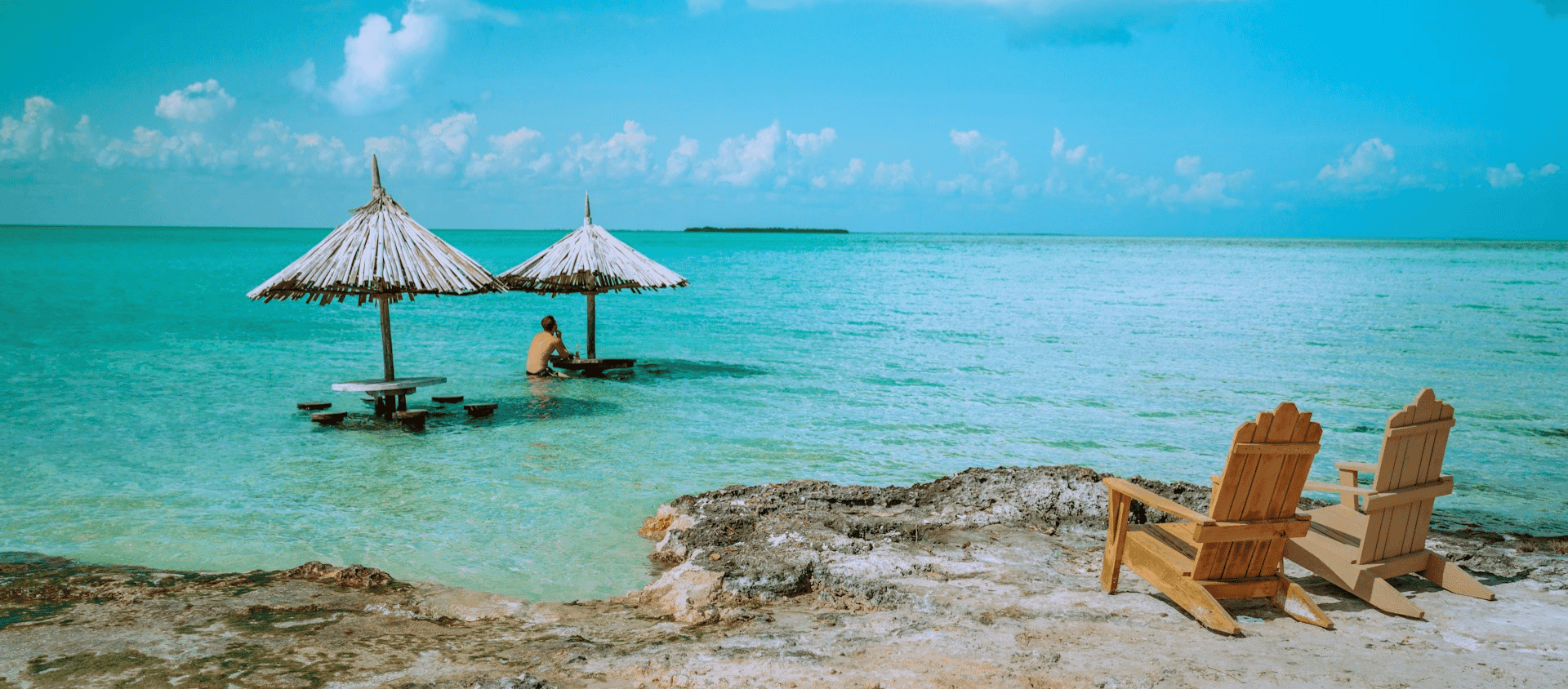 Turquoise tropical beach with thatched umbrellas and wooden chairs at a honeymoon getaway.