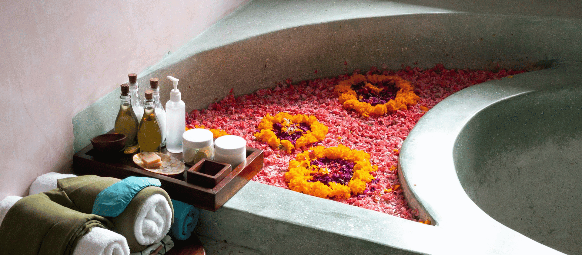 A spa bath decorated with flower petals and surrounded by skincare items.