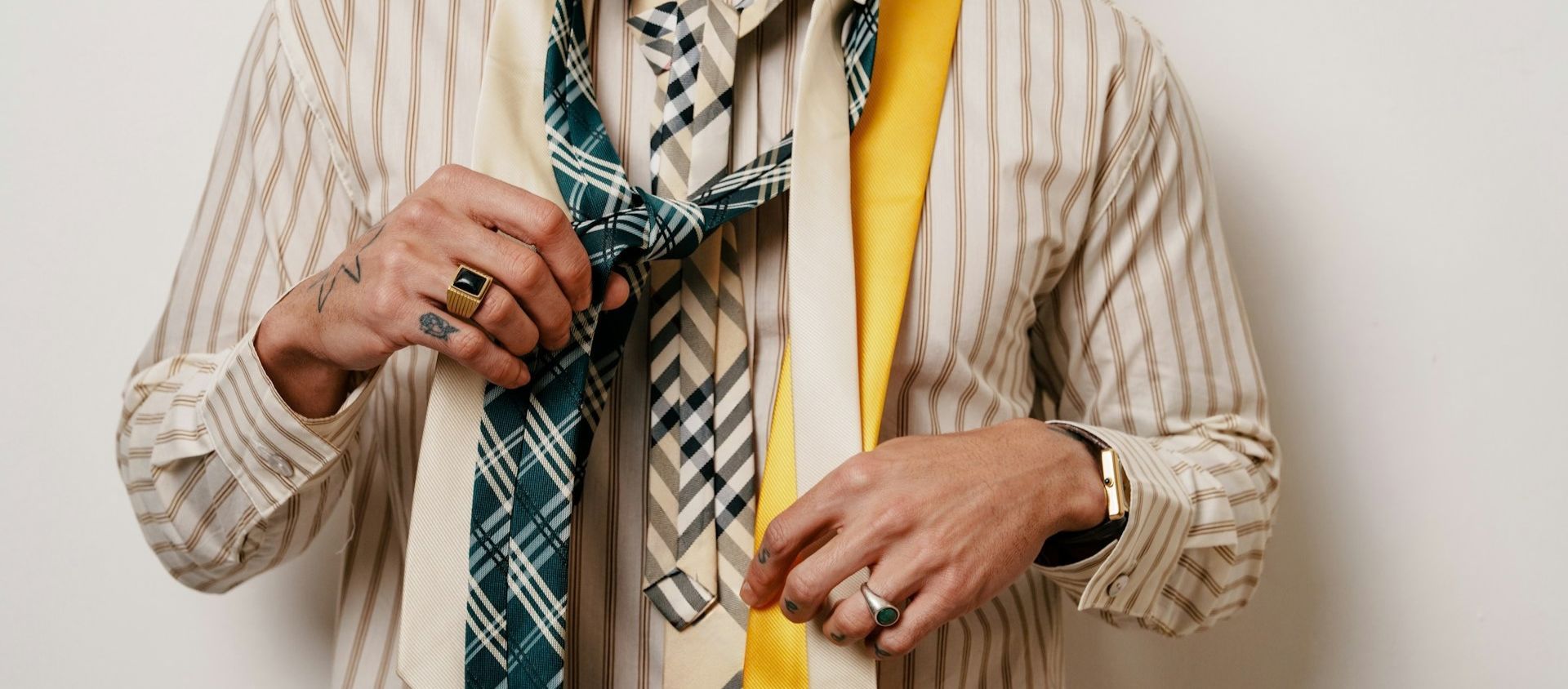 Person choosing from patterned and solid neckties while wearing rings and a watch.