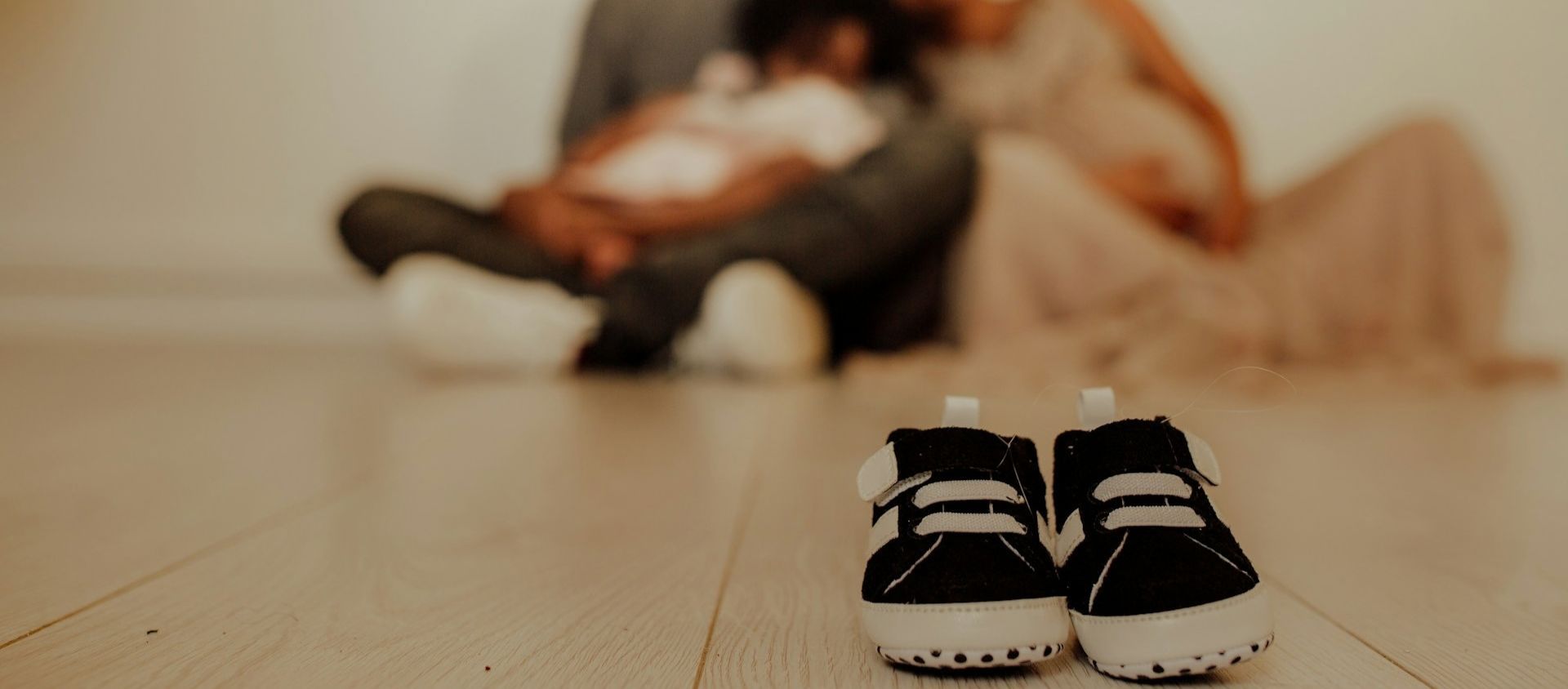 Tiny baby shoes on the floor as parents hold their newborn.