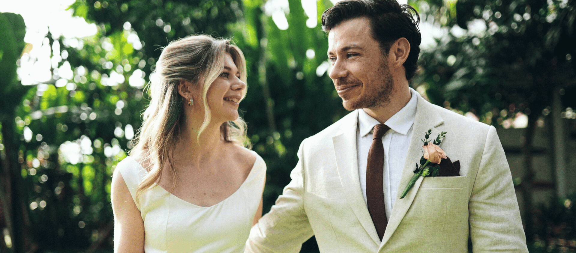 Bride and groom smiling at each other outdoors in soft natural light.