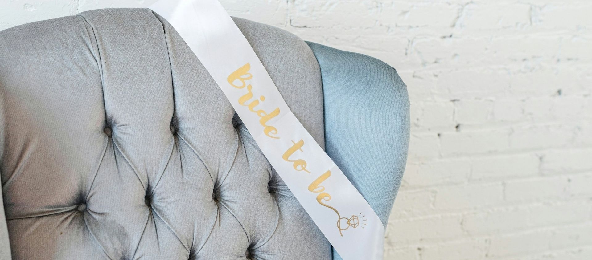 A 'bride to be' sash draped over a gray velvet armchair.