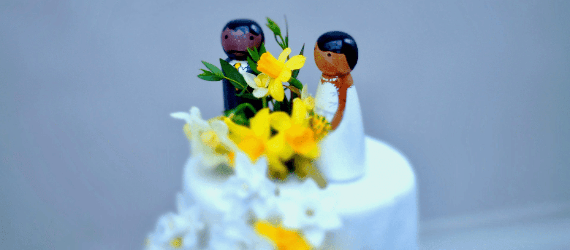 Wedding cake topped with figurines and yellow flowers.