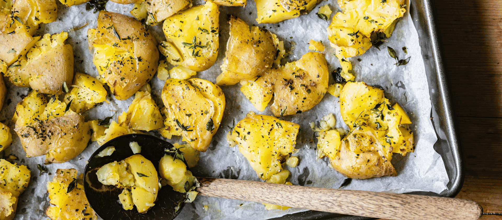 Crispy smashed potatoes on a baking tray garnished with herbs.
