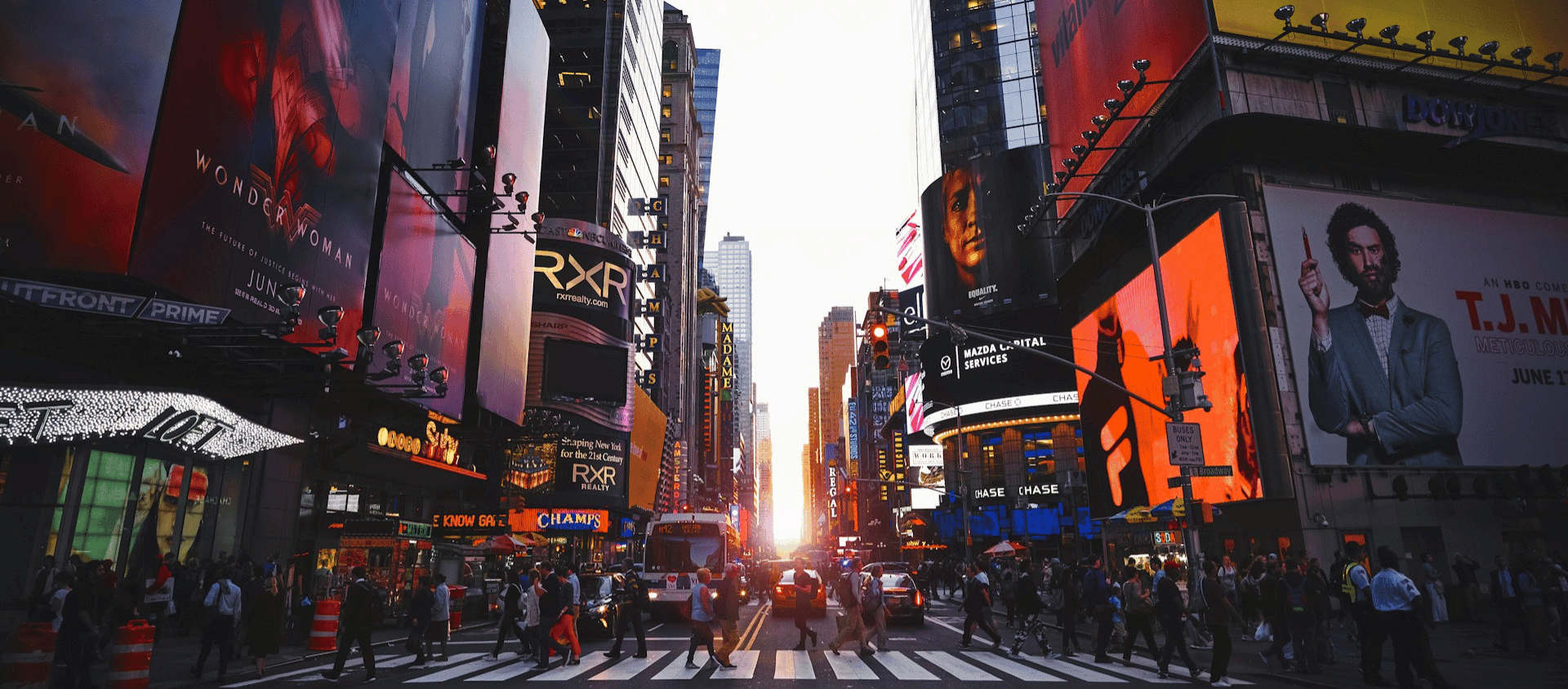Busy Times Square street in New York City with bright billboards and crowds crossing the intersection.