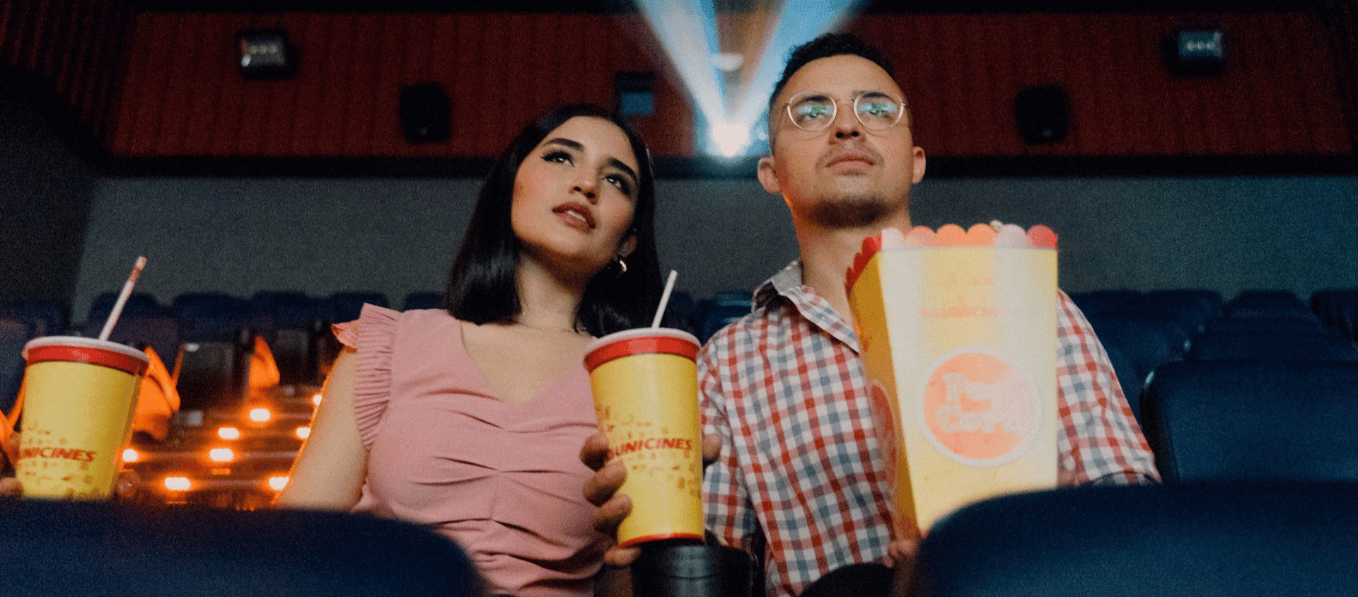 A couple sitting in a movie theater holding popcorn and drinks.