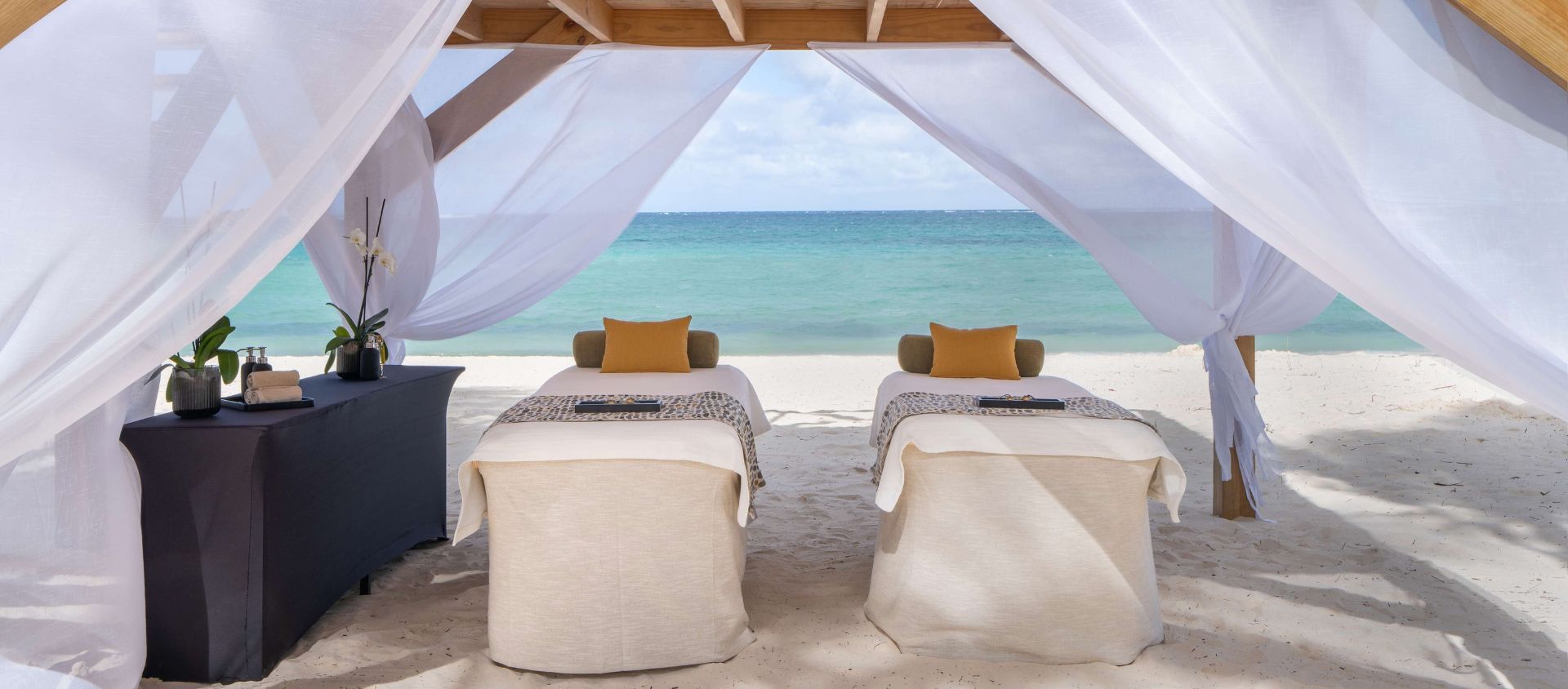 Beachfront couples spa cabana with two massage tables framed by white curtains and ocean views.