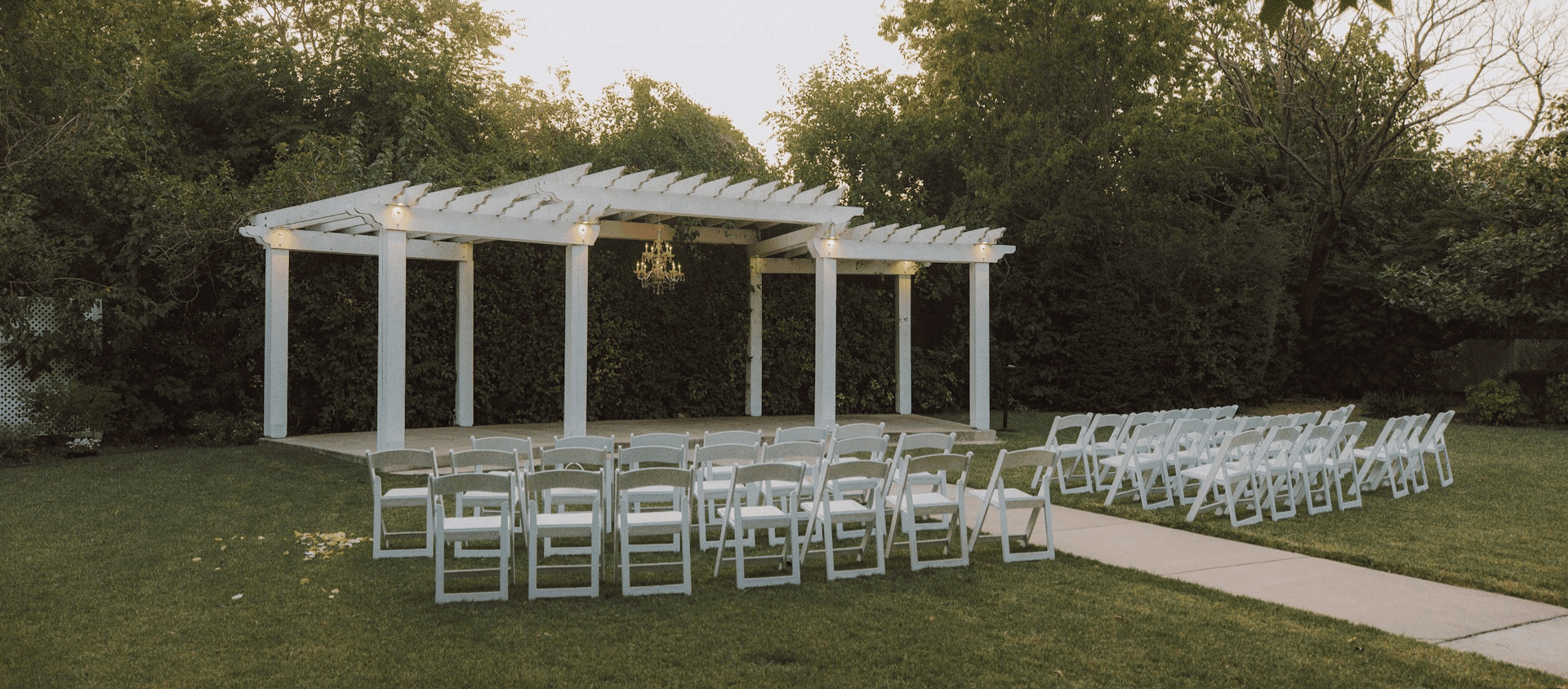 Outdoor wedding ceremony setup with white chairs and a pergola.