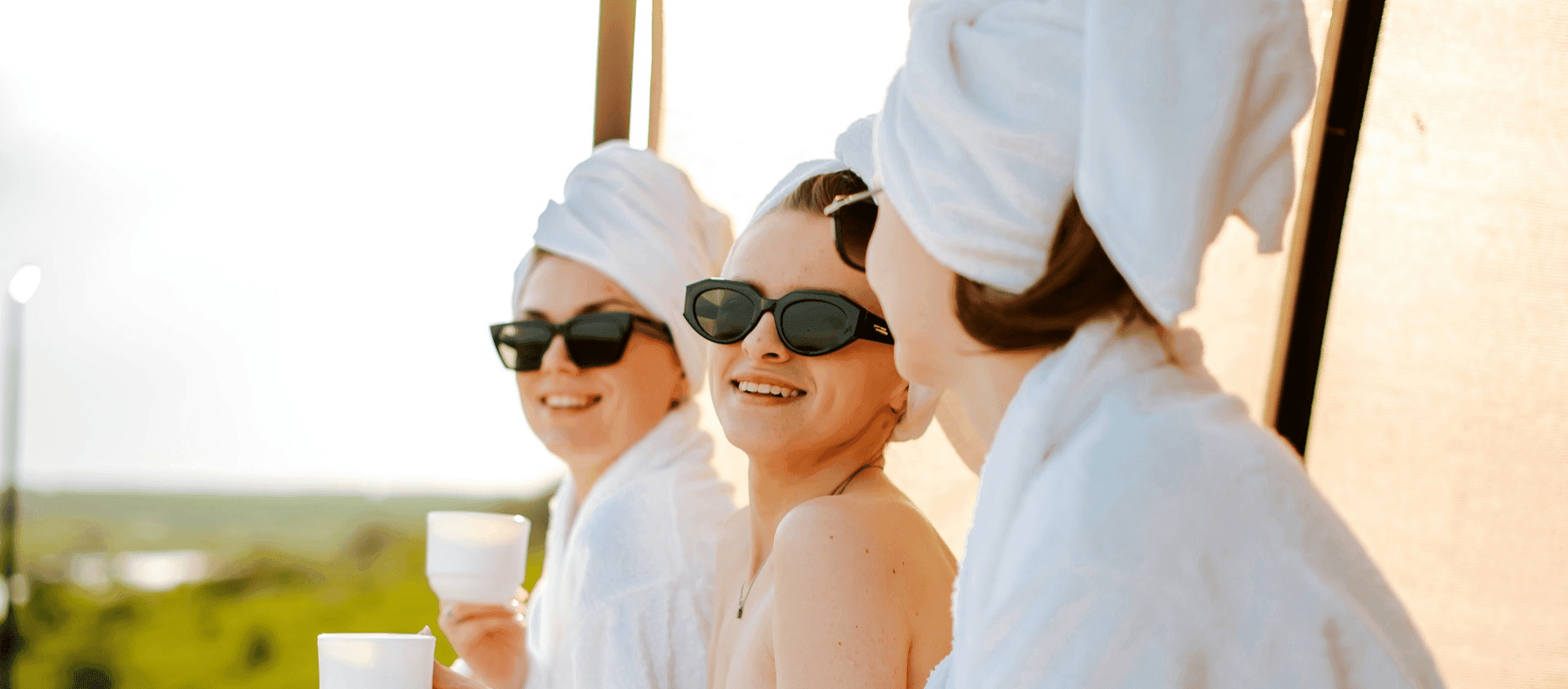 Three women in white robes and sunglasses relaxing on a hotel terrace.