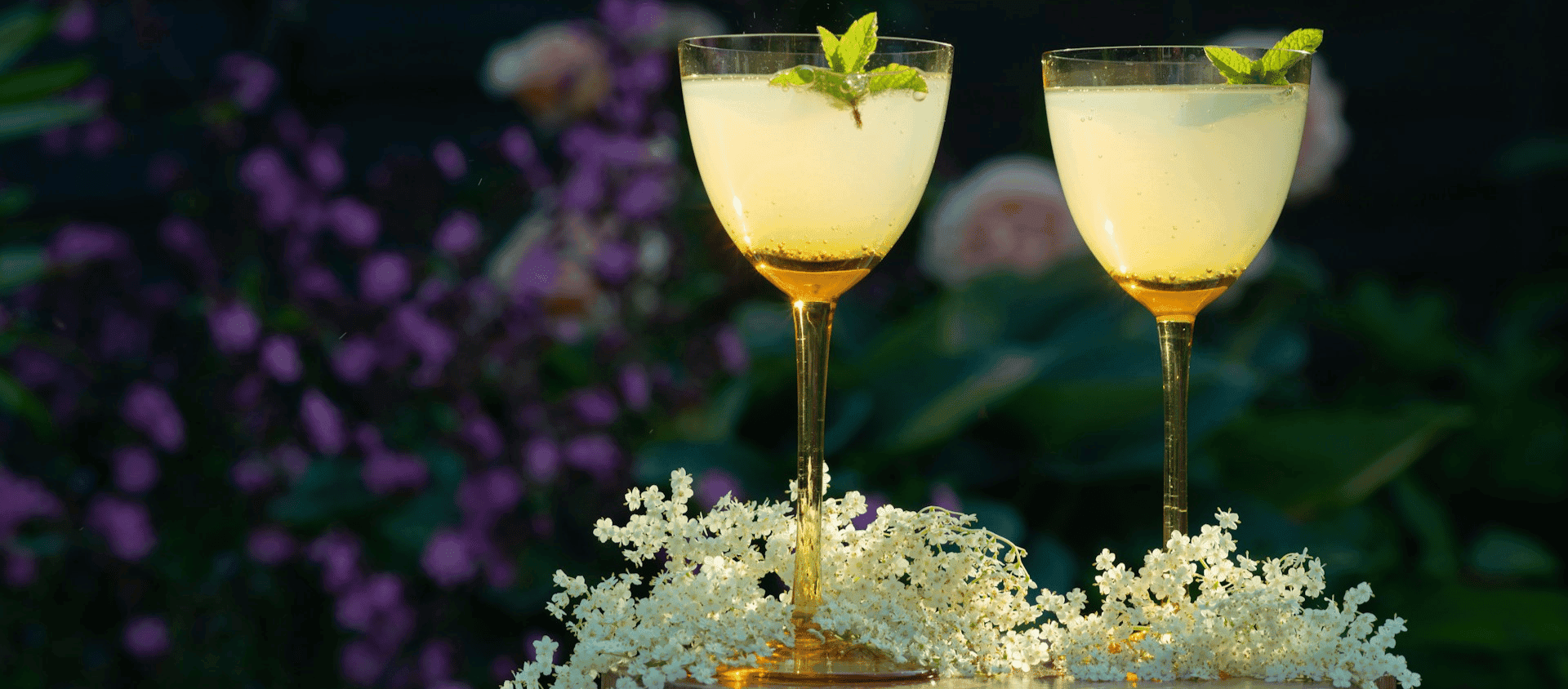 Two sparkling cocktails garnished with mint on a floral-decorated table.