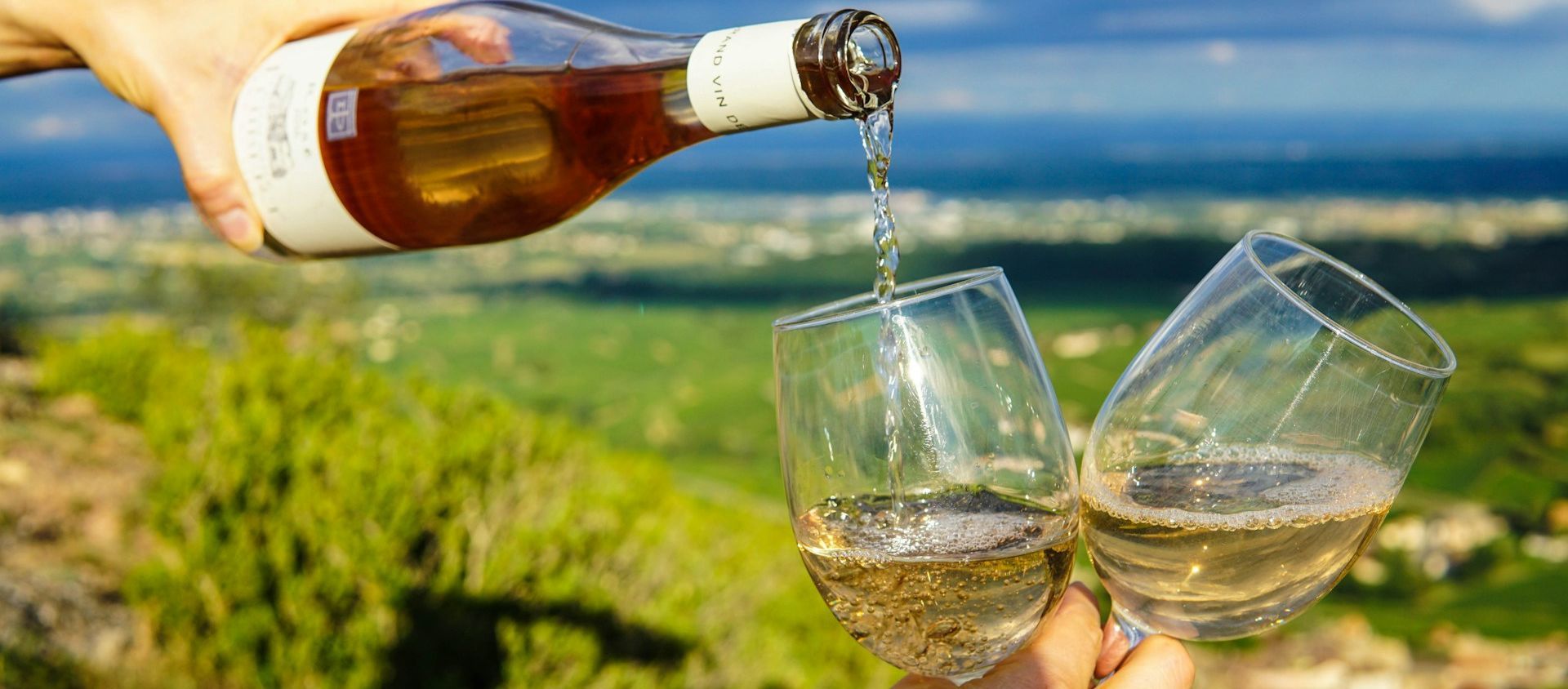 Two glasses of wine being poured with a vineyard view.