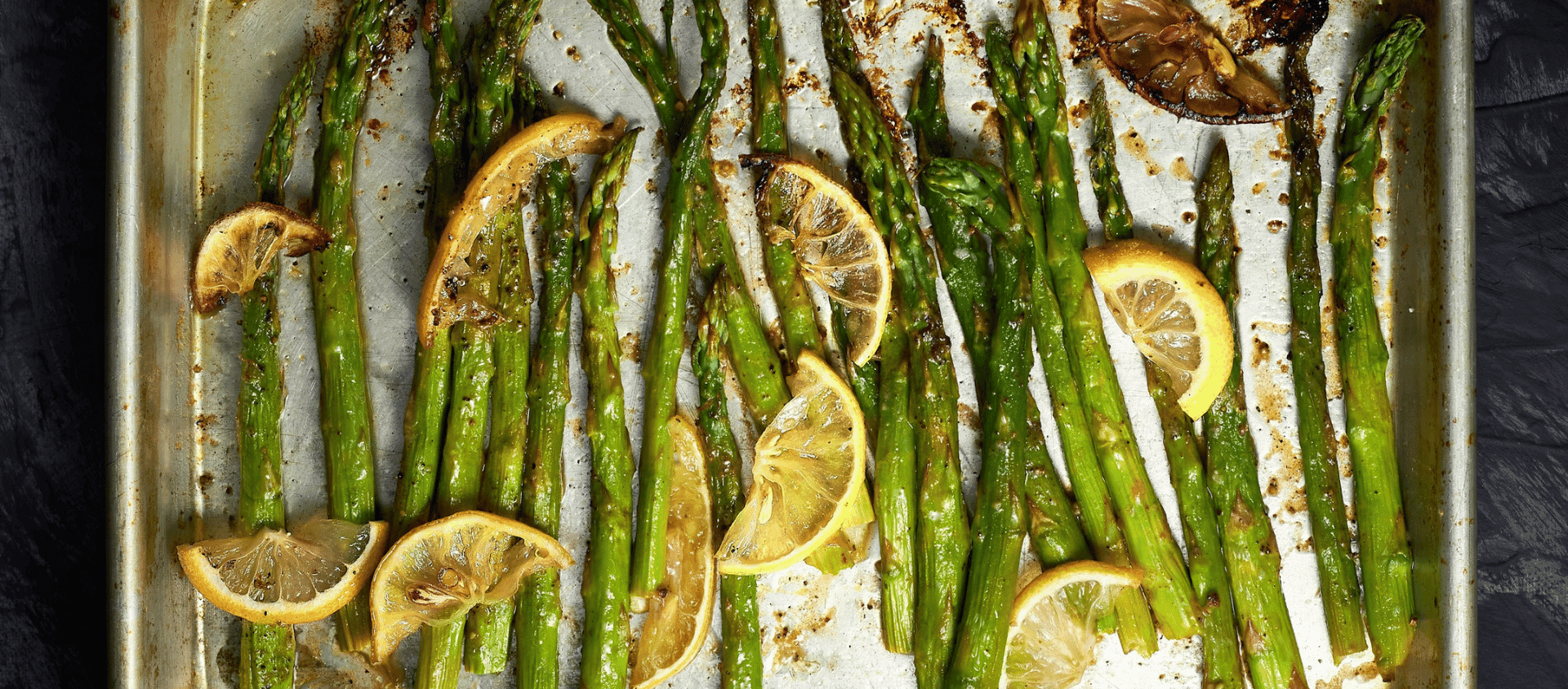 Roasted asparagus with brown butter and lemon slices arranged on a tray.