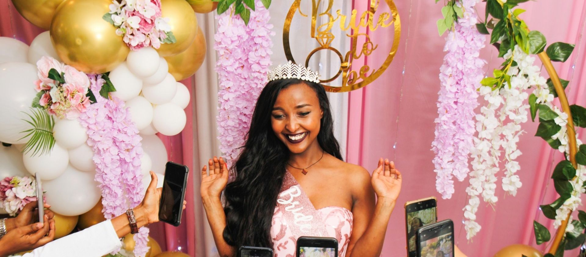 A bride-to-be in a tiara and sash smiles at her bridal shower.
