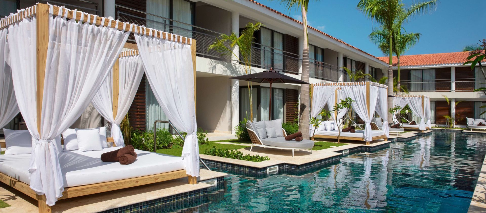 Poolside daybeds with white curtains lining a resort pool at a Punta Cana resort.