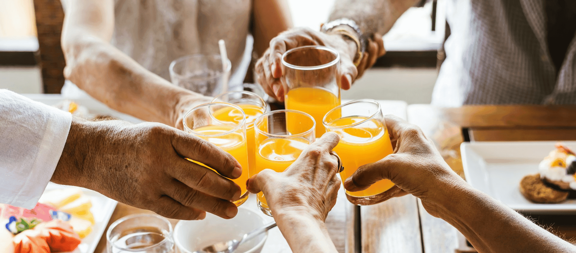 Group of hands clinking mimosa glasses together at a birthday brunch.
