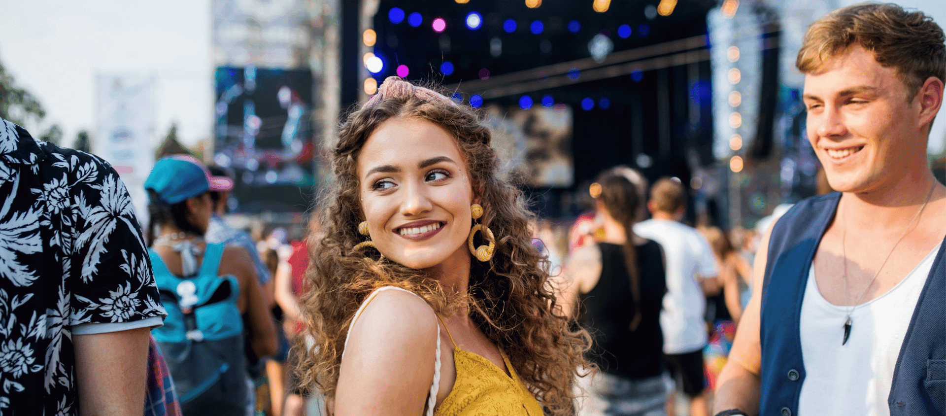 A woman smiling at an outdoor concert with a crowd behind her.