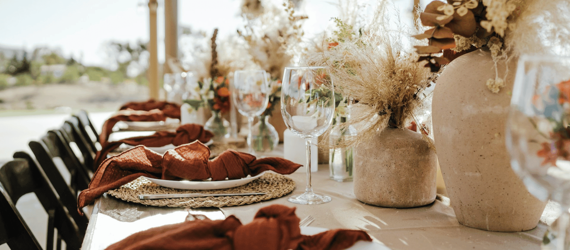 Rustic outdoor reception table with glassware, vases, and warm-toned linens.