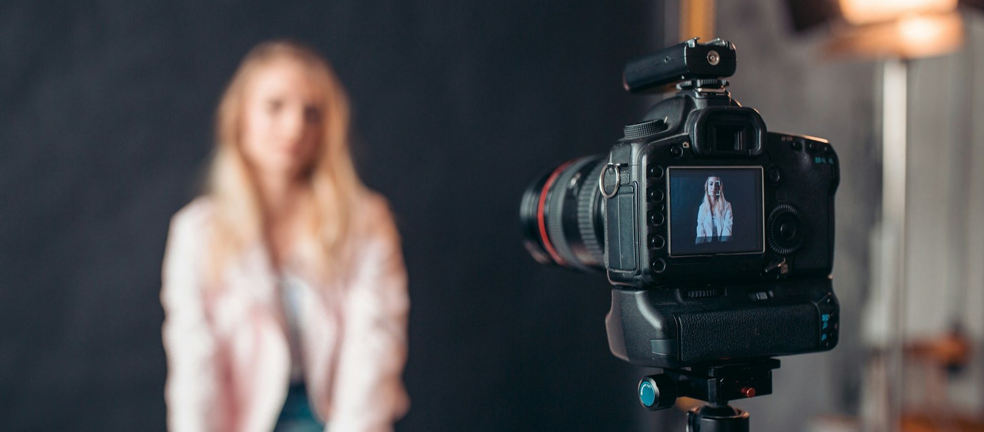 Camera on a tripod photographing a person in a studio.