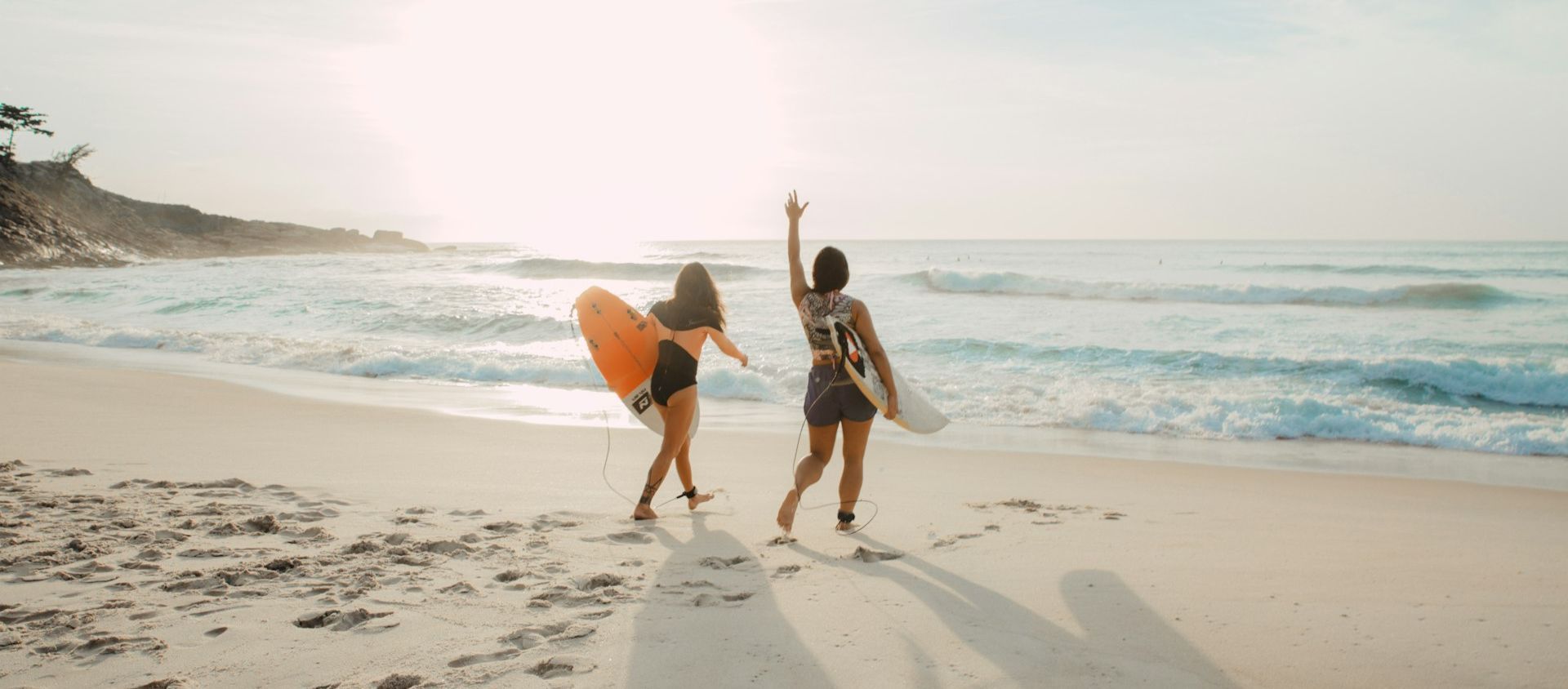 Two friends walking on the beach carrying surfboards at sunset.