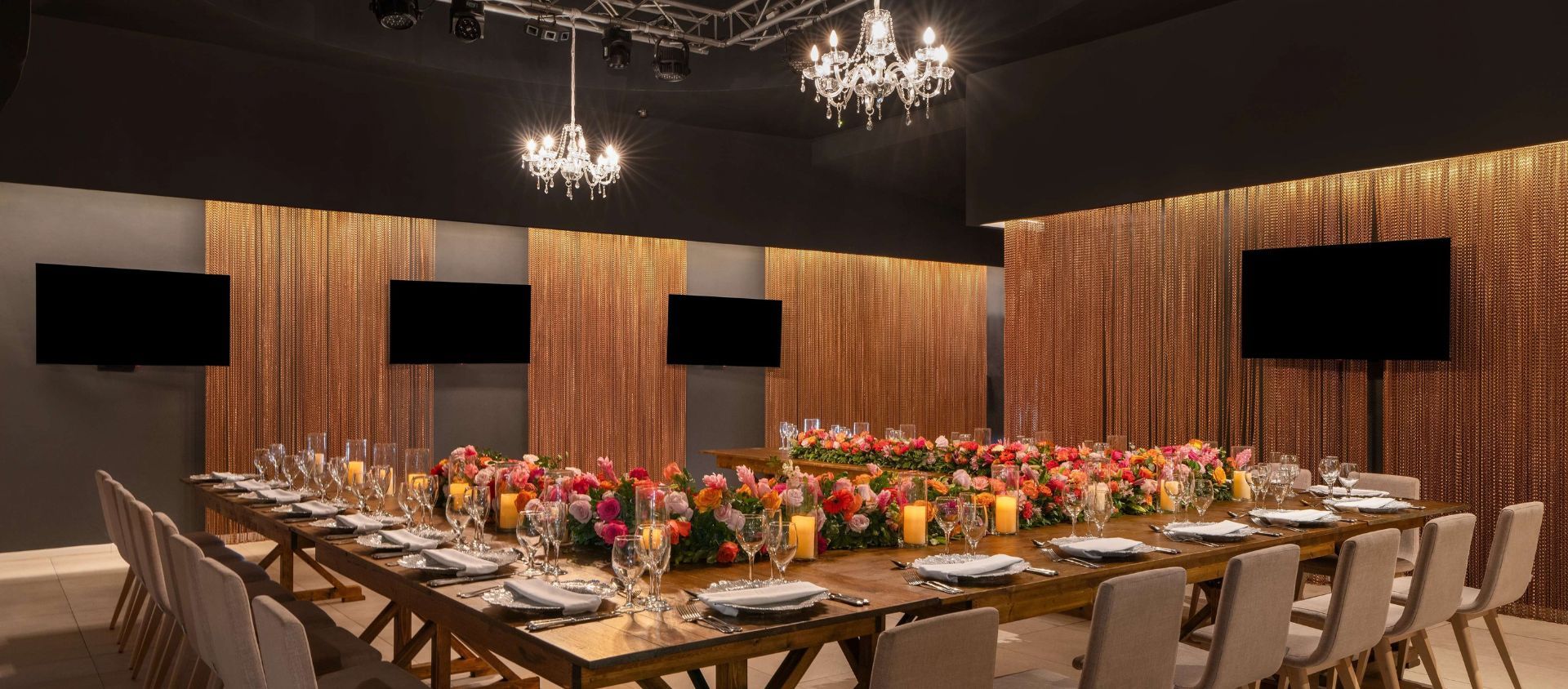 Elegant indoor reception with crystal chandeliers and a long table with vibrant floral centerpieces.