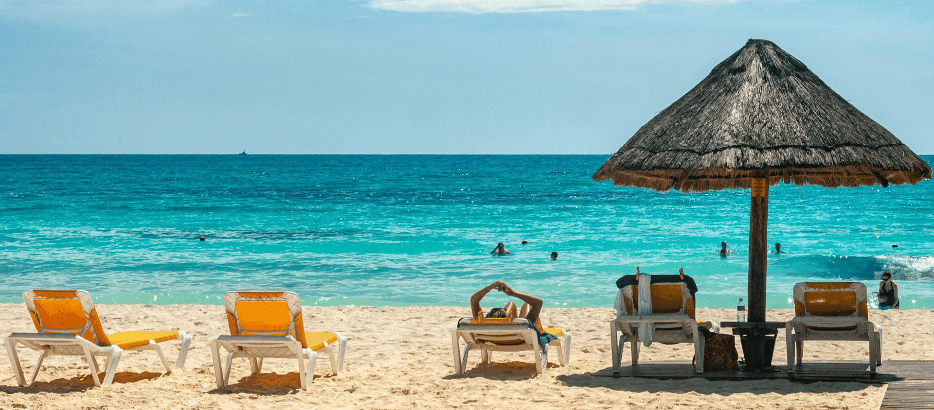 Beach chairs and an umbrella in Cancún facing turquoise ocean waves on a sunny day.