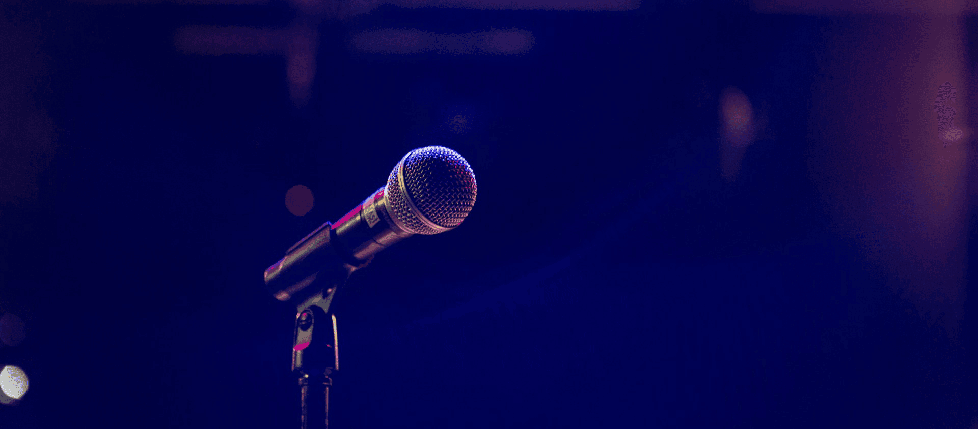 Microphone on a stand under stage lighting against a dark background.