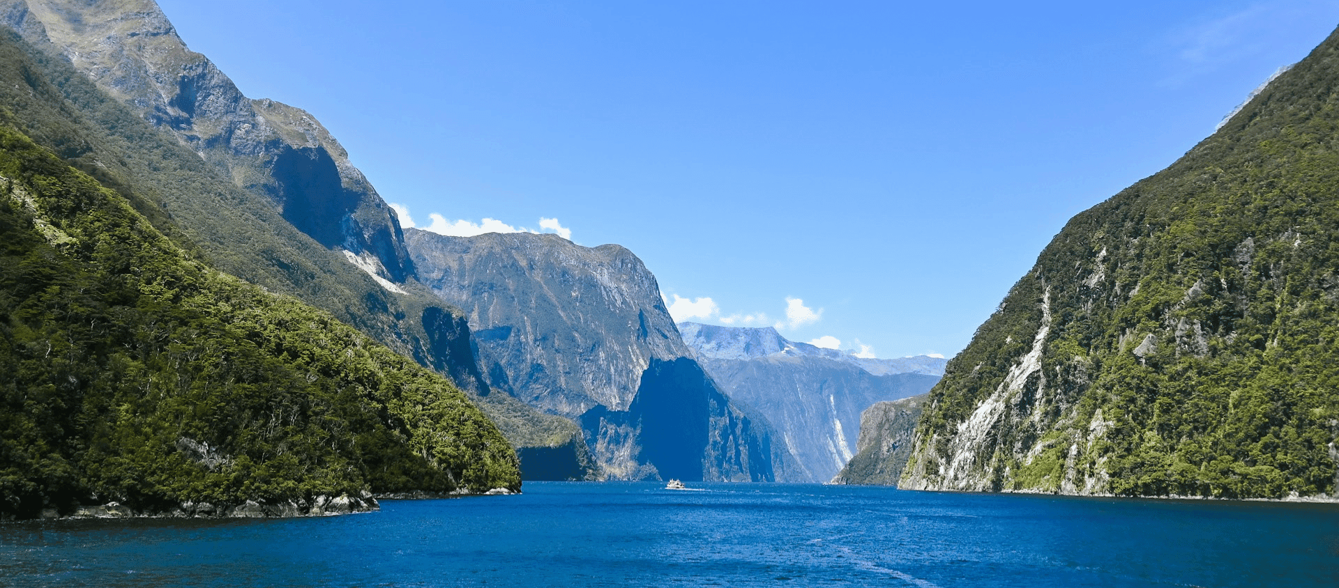 Blue water surrounded by steep green mountains under a clear sky.