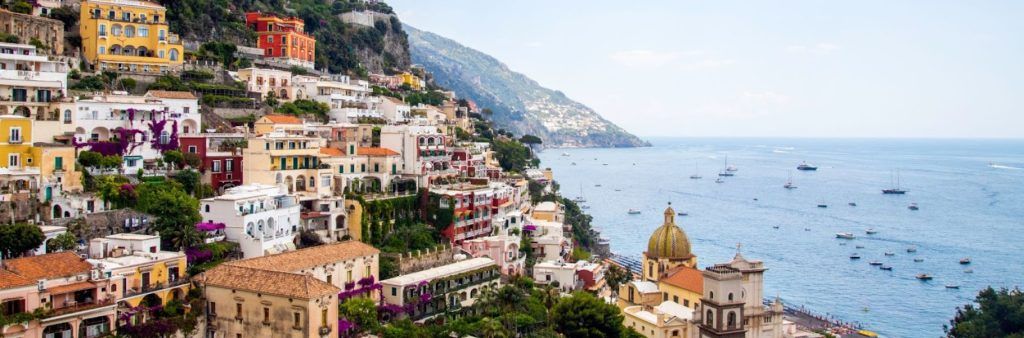 Colorful hillside buildings in Positano overlooking the Amalfi Coast and the sea dotted with boats.