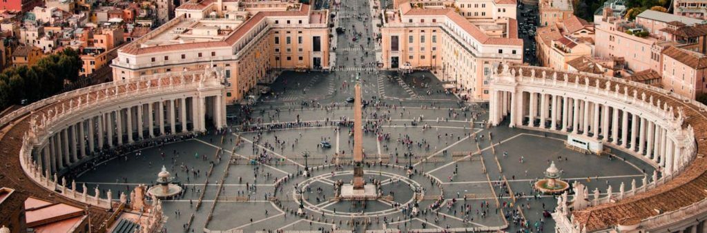 Aerial view of St. Peter’s Square in Vatican City with crowds gathered around the central obelisk and colonnades.