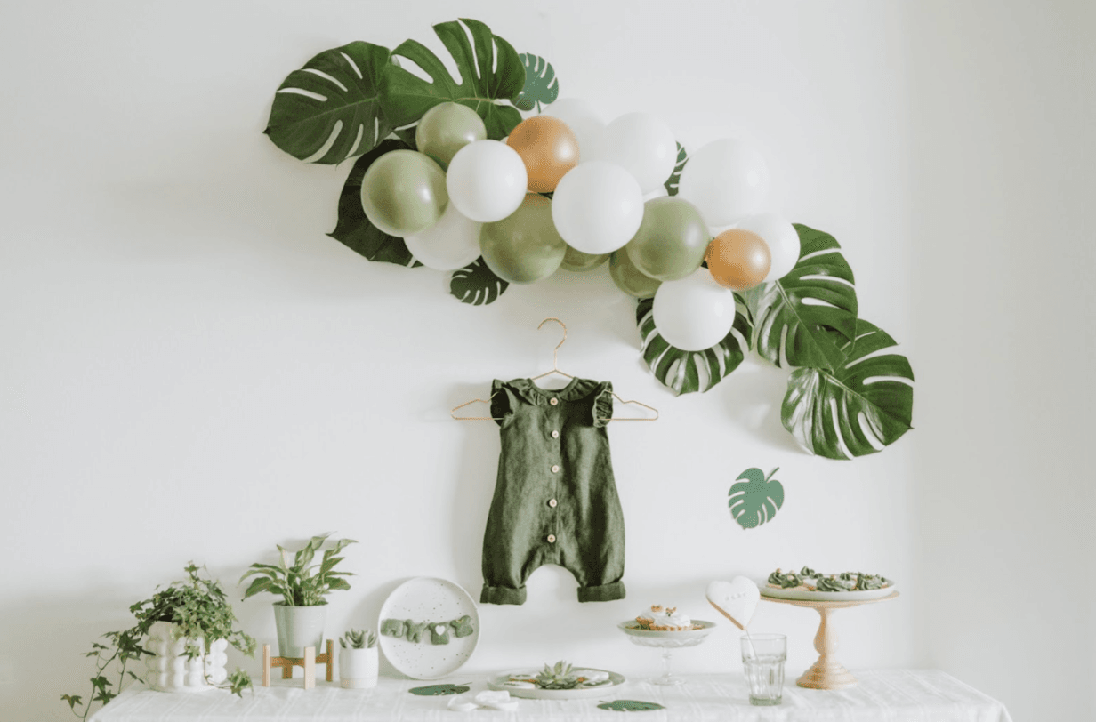 Green and white baby shower decor with balloons and outfit display.