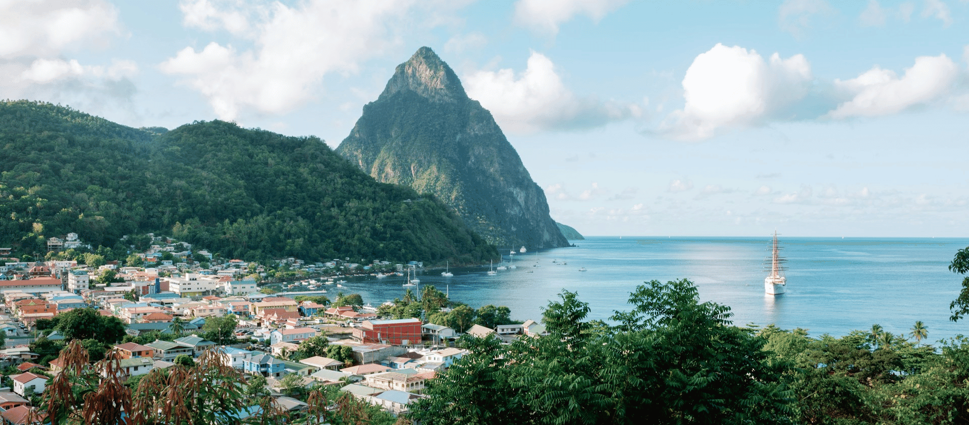 Coastal town below a dramatic mountain peak overlooking calm blue water and anchored boats.