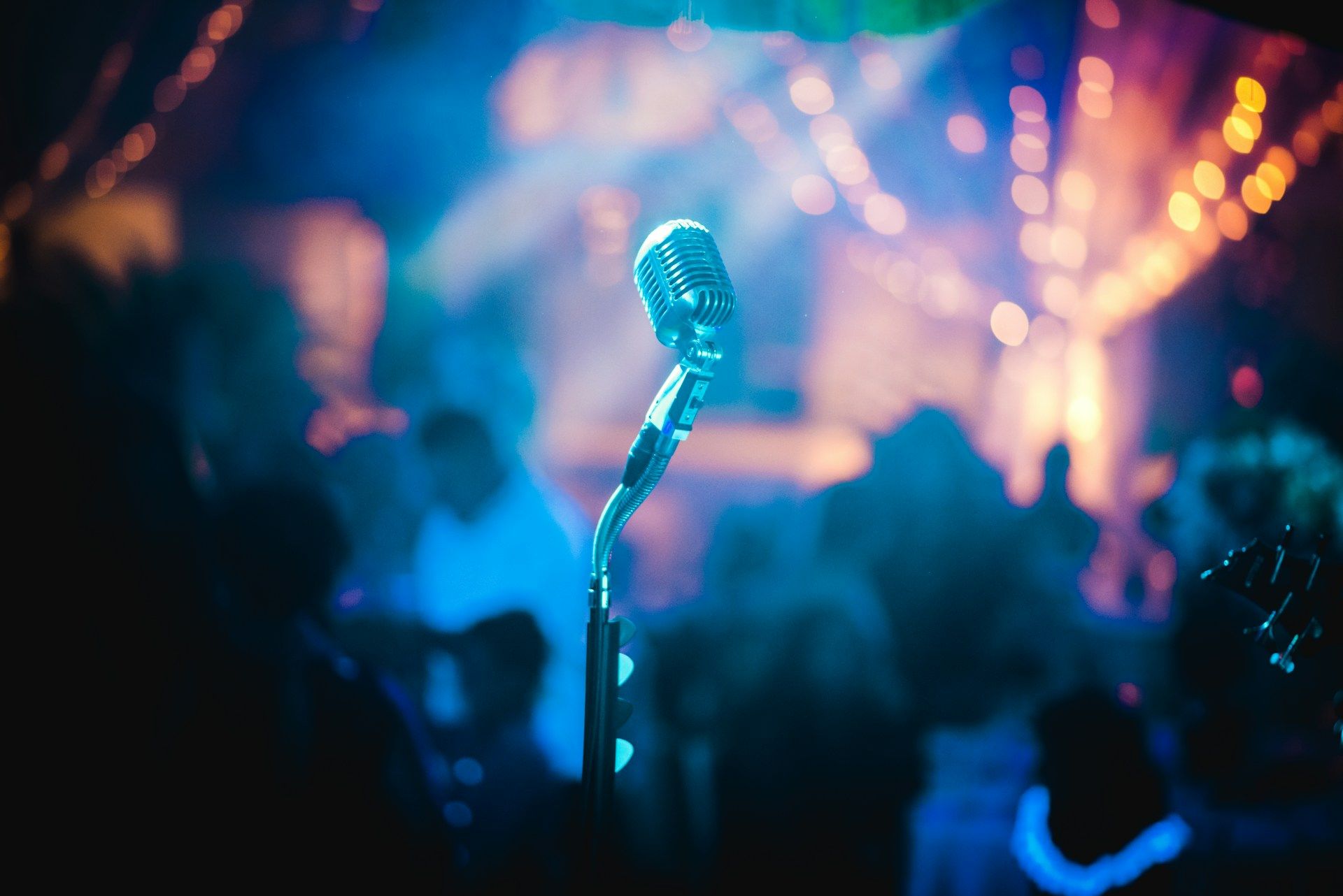 Vintage microphone on stage with blurred audience and colorful lights.