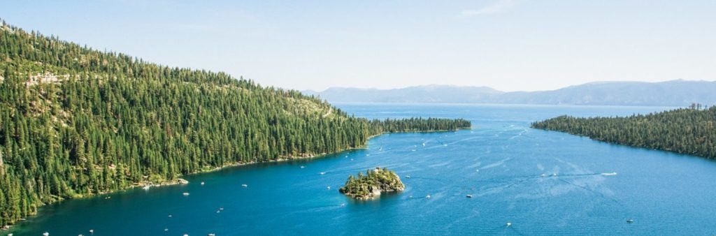 Aerial view of a blue lake surrounded by forested mountains with a small island near the shore.