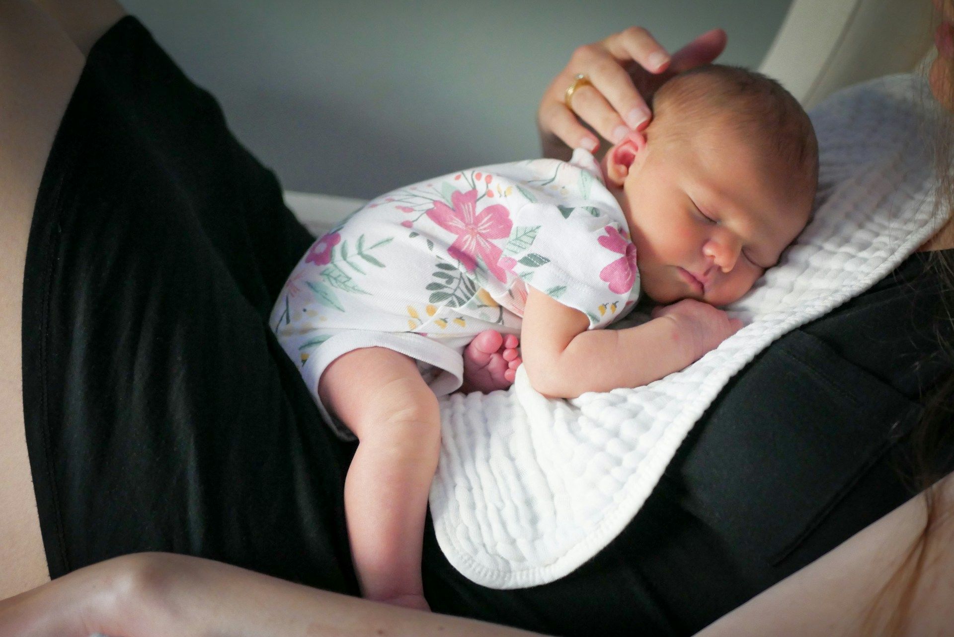 Sleeping newborn in a floral onesie resting on a nursing pillow