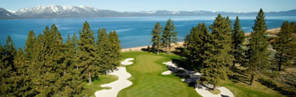 Golf course green surrounded by pine trees overlooking Lake Tahoe and distant snow-capped mountains.