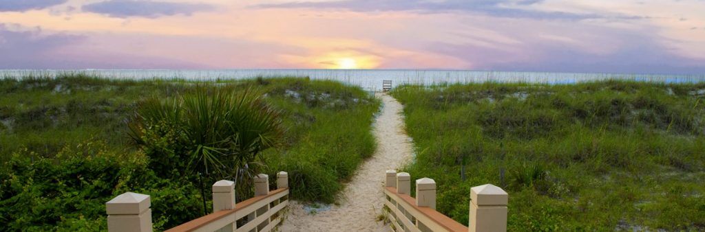 Sandy pathway at Hilton Head, South Carolina through grassy dunes leading to the beach at sunset.