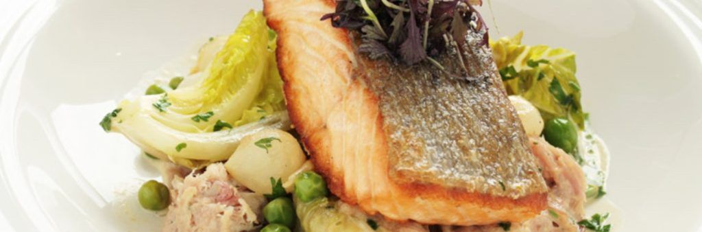 Seared salmon fillet served over vegetables and potatoes, garnished with greens.