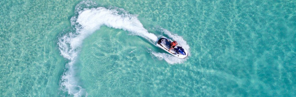 Person riding a jet ski across clear turquoise water, leaving a white wake behind.