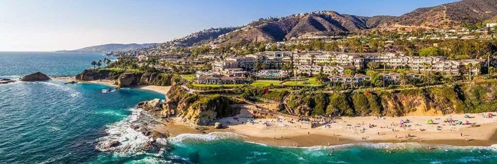 Aerial view of a coastal resort in Laguna Beach with turquoise waves and hills in the background.