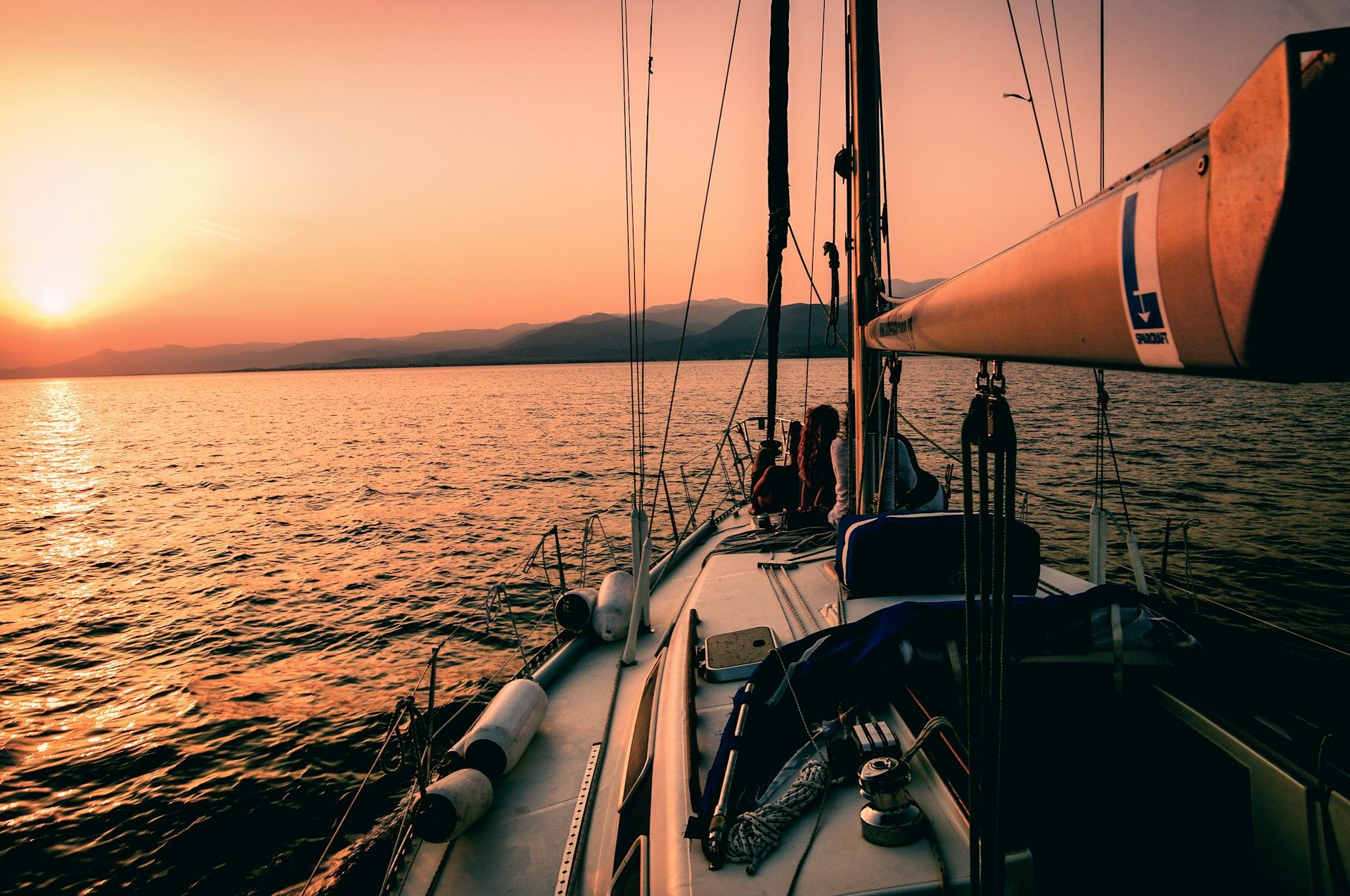 Couple relaxing on a sailboat while watching the sunset over the water.