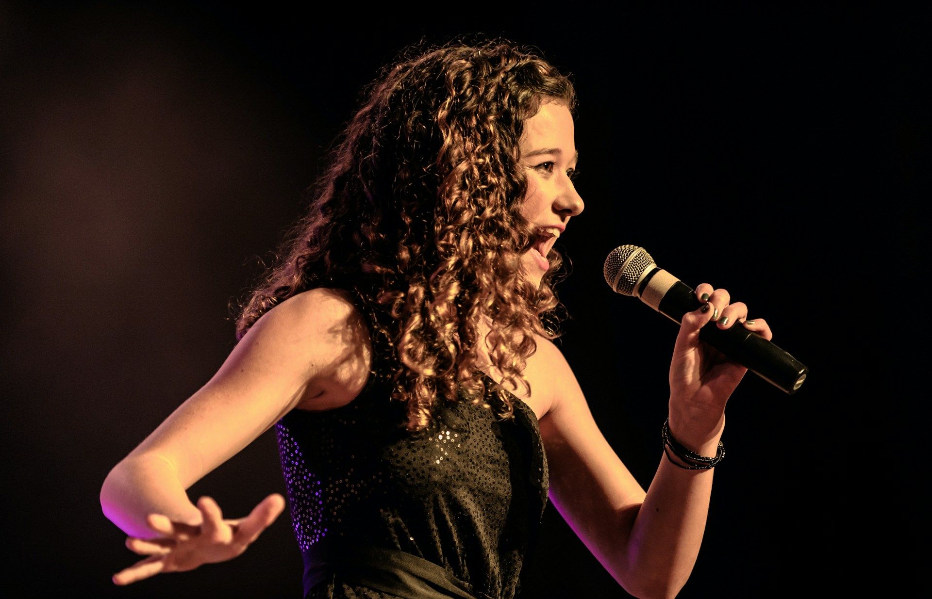 Young woman singing into a microphone on stage.