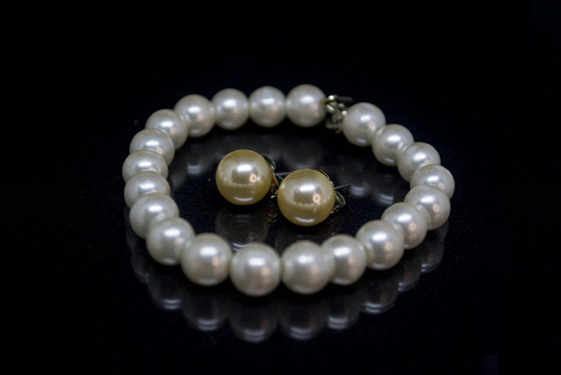 Pearl bracelet with matching pearl stud earrings on a black background.