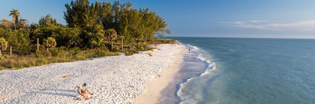 White sand beach on Sanibel Island, Florida, bordered by turquoise water and lush greenery.