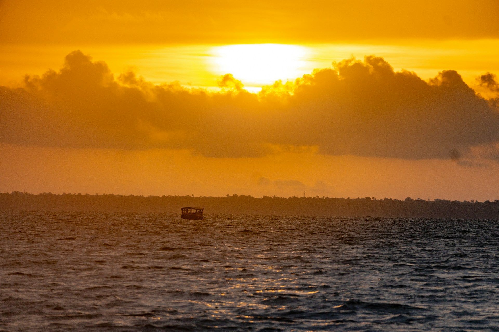Small boat on the ocean at sunset with golden sky and clouds on the horizon.