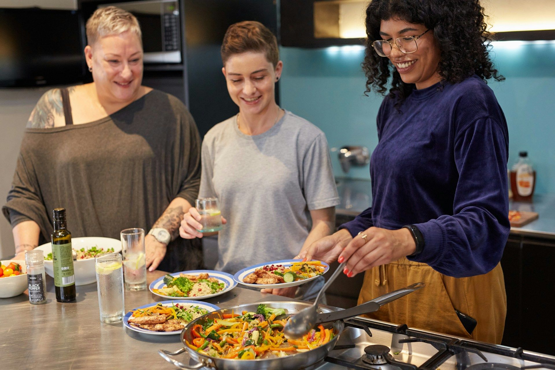Three women plating a healthy meal in a modern kitchen.