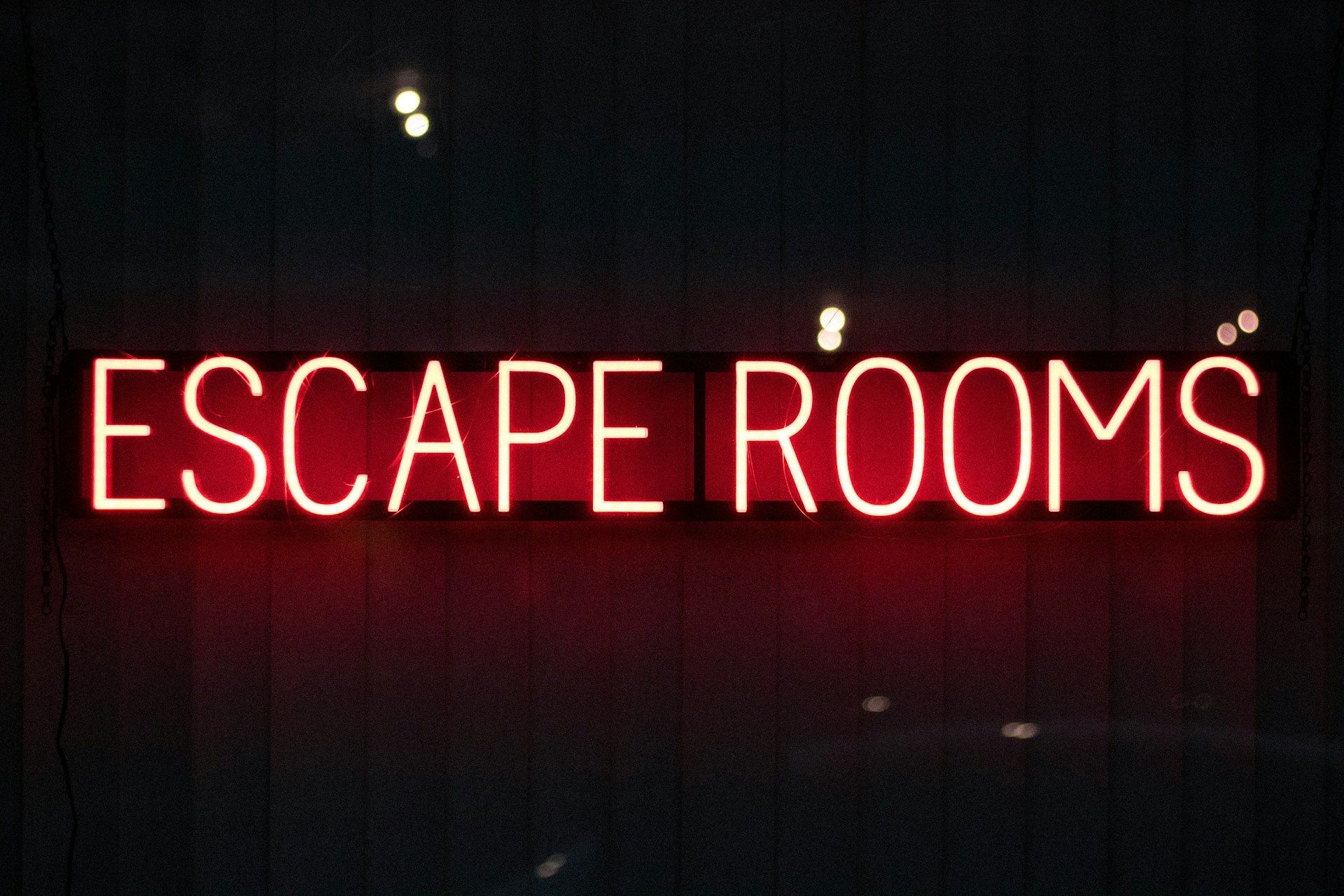 Red neon “ESCAPE ROOMS” sign on a dark wall.